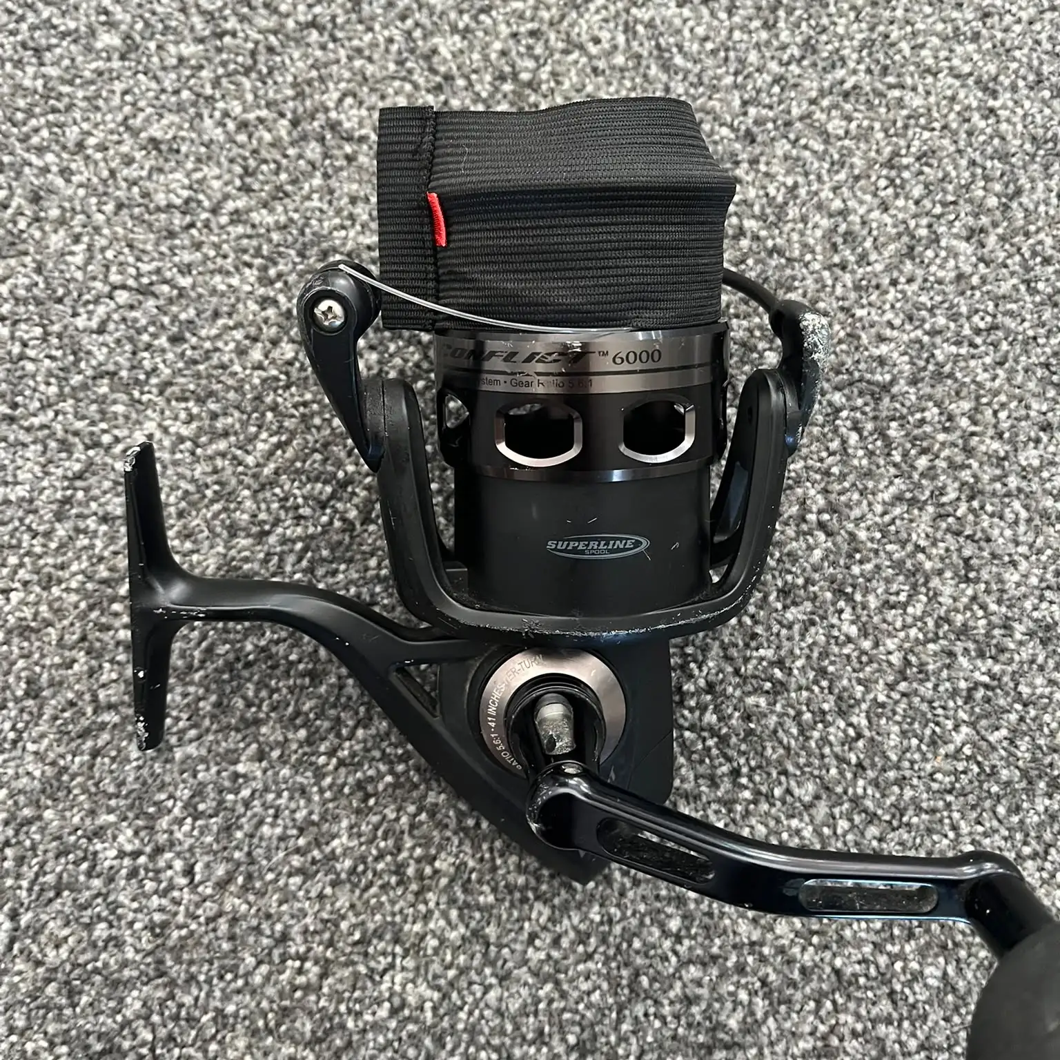 Used Penn Conflict 6000 spinning reel from the front, showing the spool label and scratches on the reel foot and bail arm